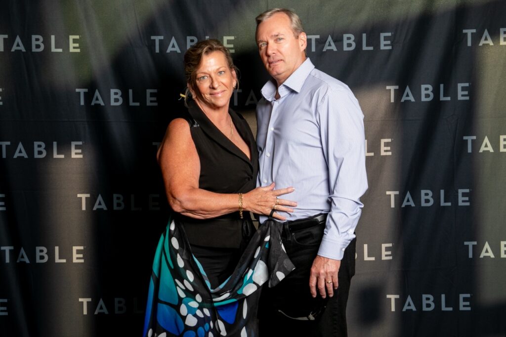 Couple posing in front of a "TABLE" backdrop at an event.
