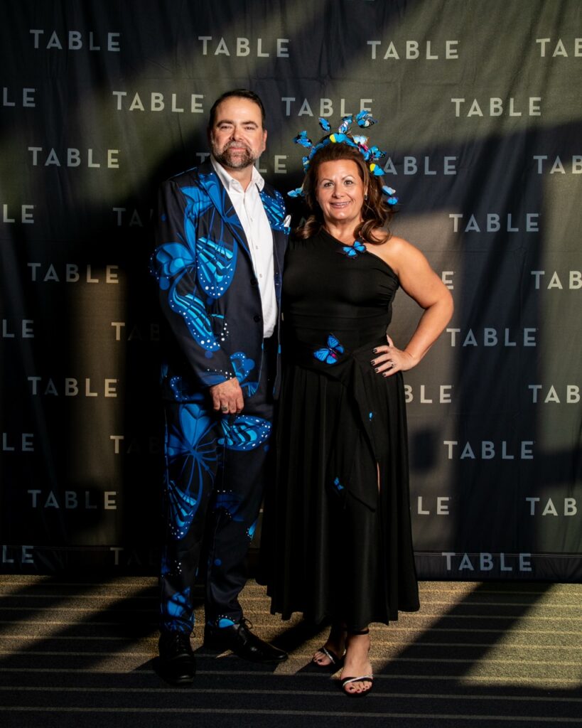 Couple in butterfly-themed outfits at an event with "TABLE" backdrop