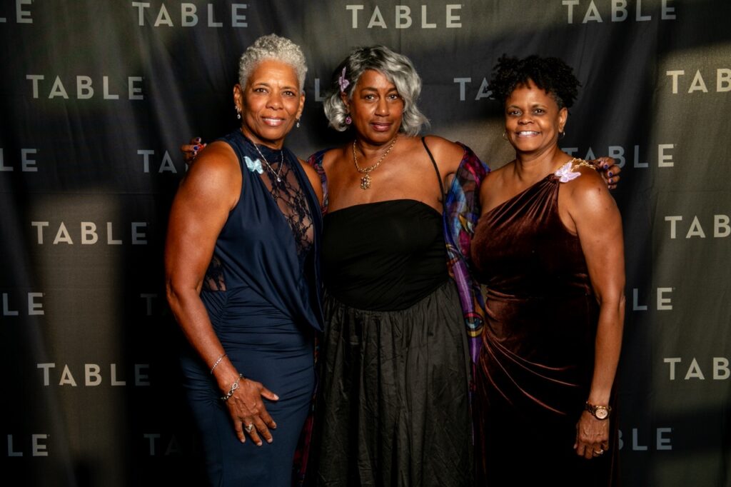 Three women pose for a photo at an event with a "TABLE" backdrop.