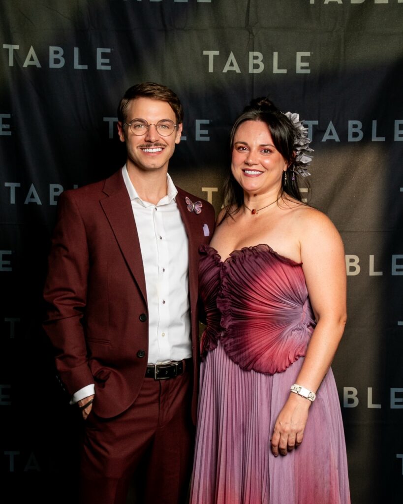 Couple posing in front of a black backdrop with "TABLE" logo.