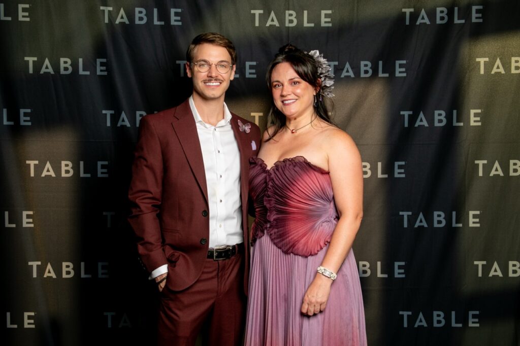 Man in maroon suit and woman in purple gown pose for photo at TABLE event.