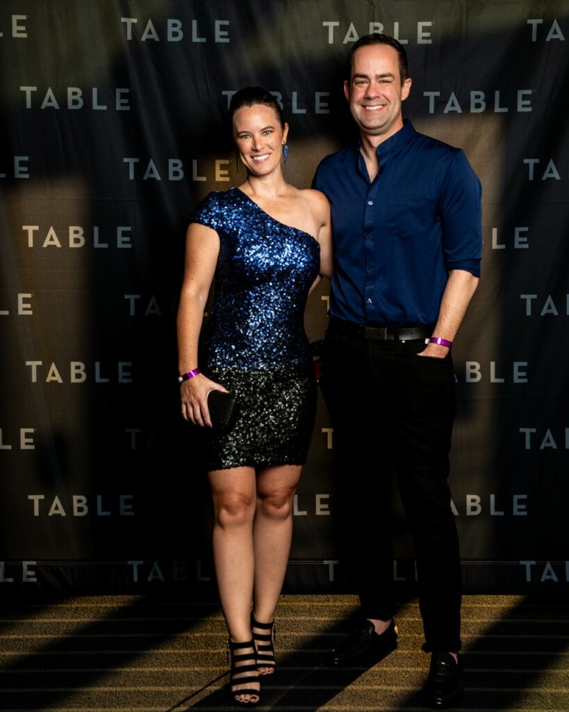 Couple posing in front of a backdrop with the word "TABLE" repeated.