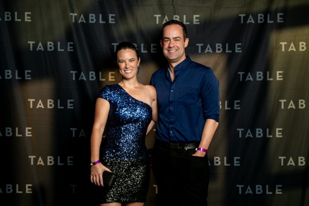 Couple posing in front of a "TABLE" backdrop at an event