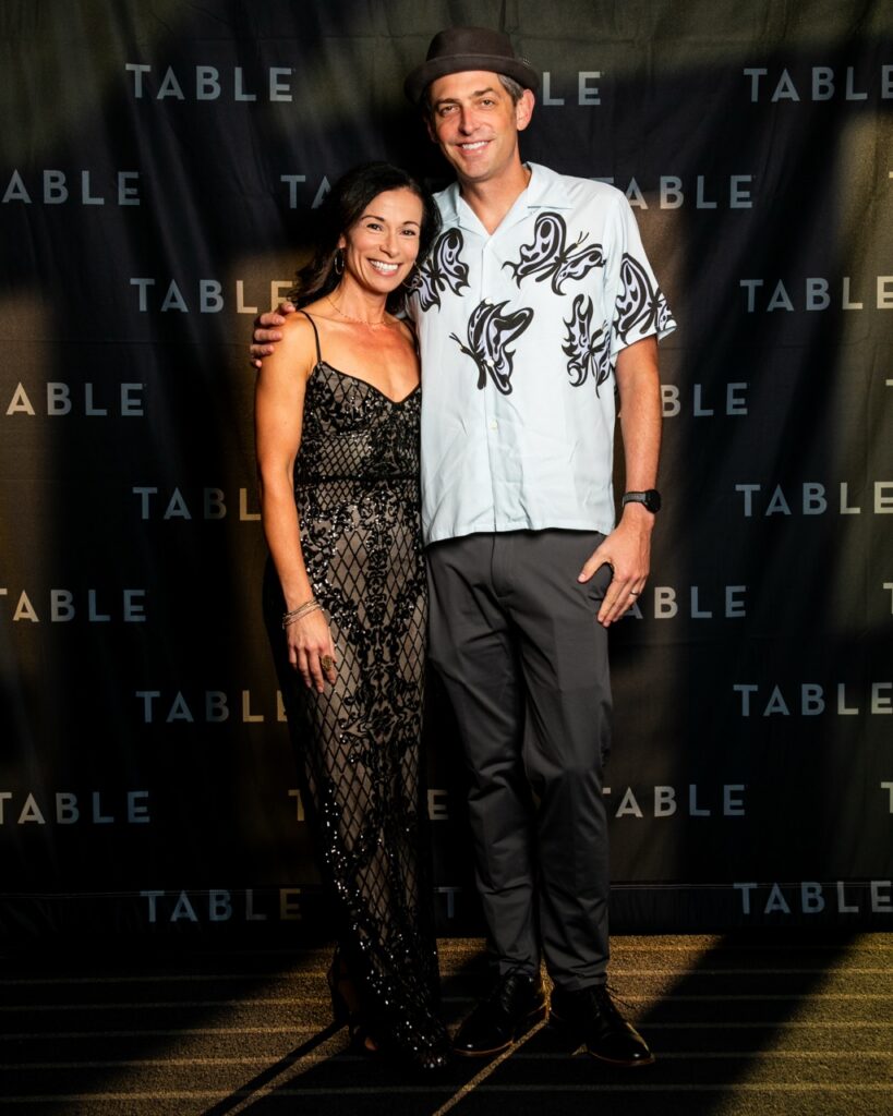 Couple posing for photo at TABLE event with "TABLE" logo backdrop