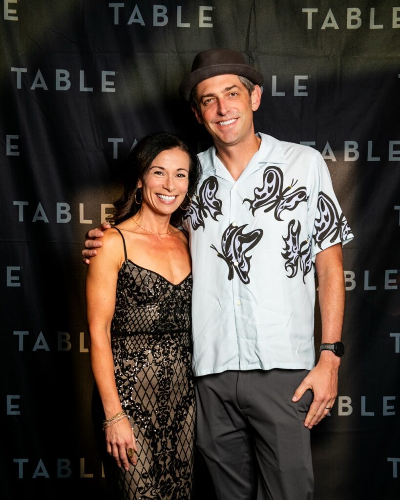 Couple posing in front of a black backdrop with "TABLE" logo