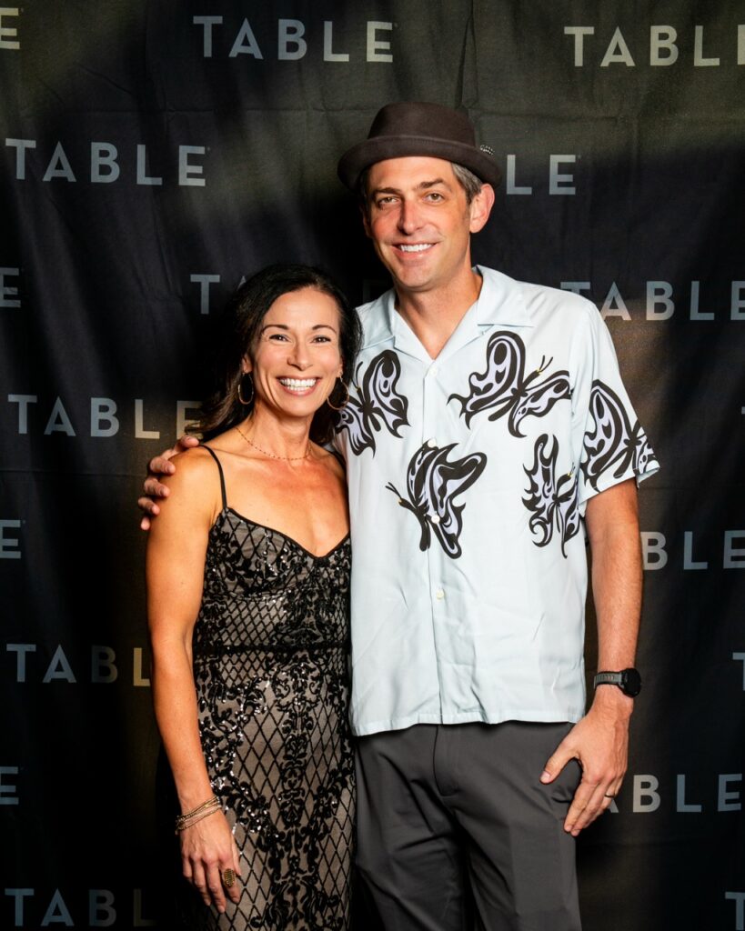 Couple smiling in front of a black backdrop with "TABLE" logo