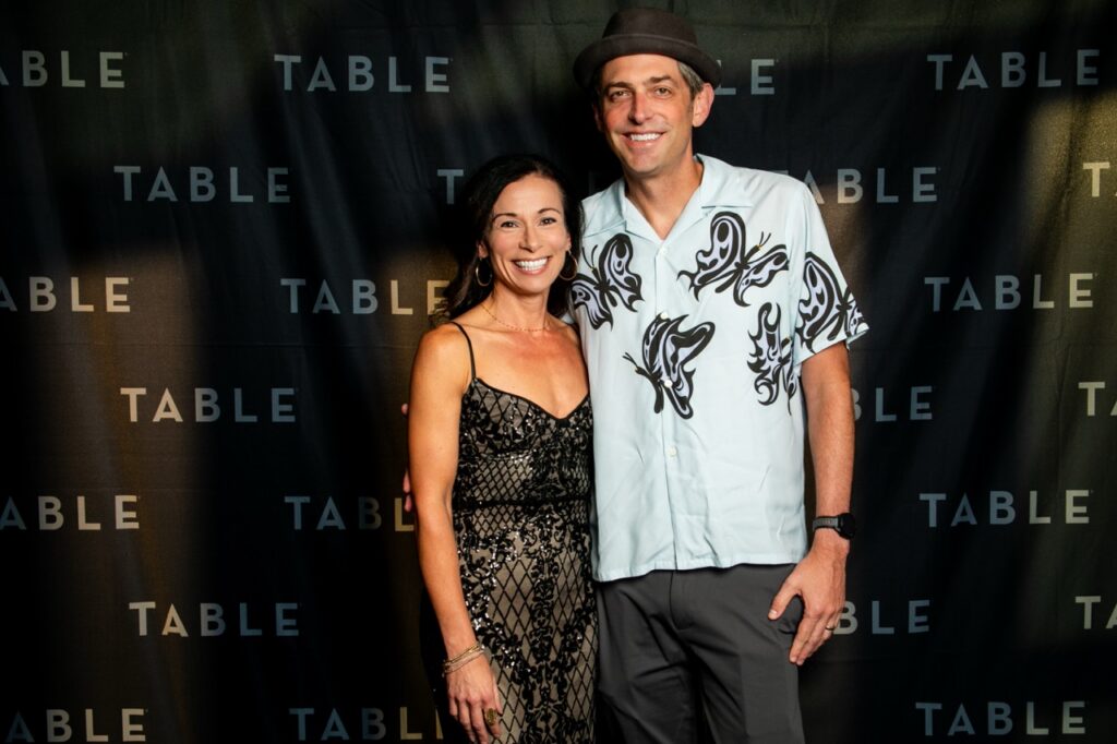 Couple posing for a photo at an event with a "TABLE" backdrop.