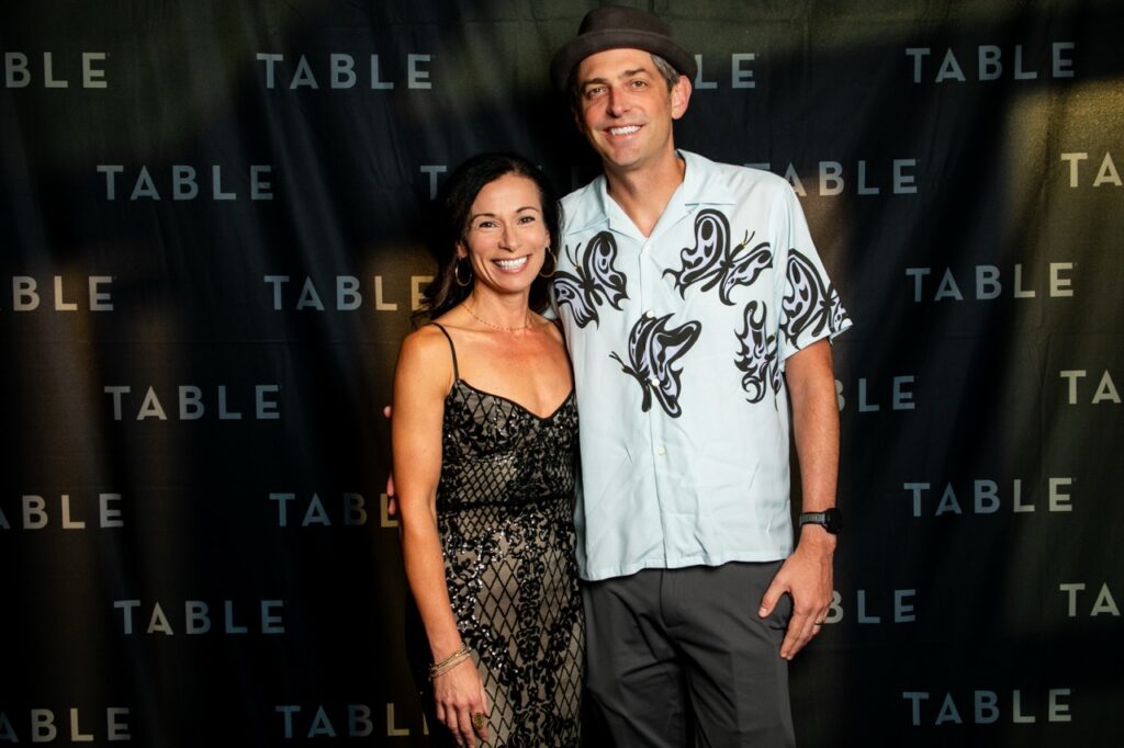 Man in butterfly shirt and woman in sequin dress pose for TABLE event photo
