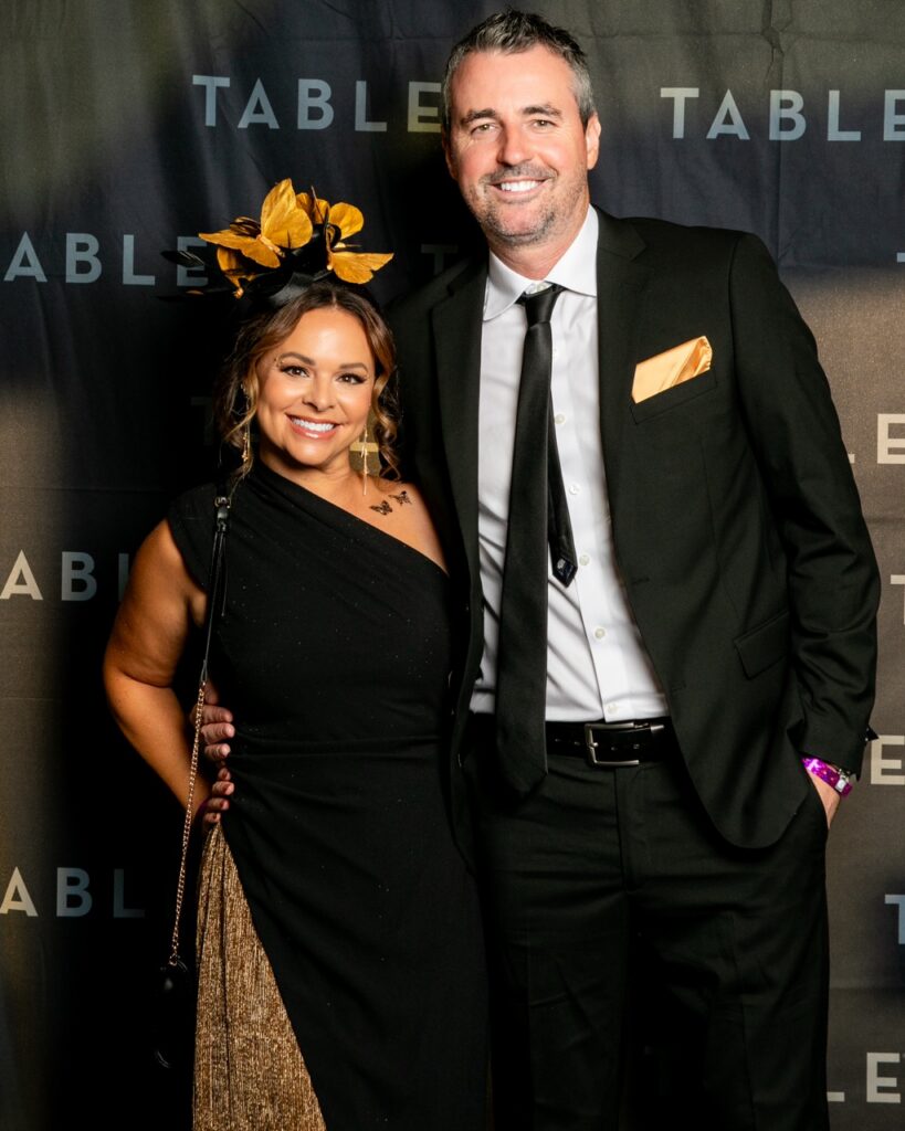 Couple in formal wear at a TABLE event, woman wears a fascinator