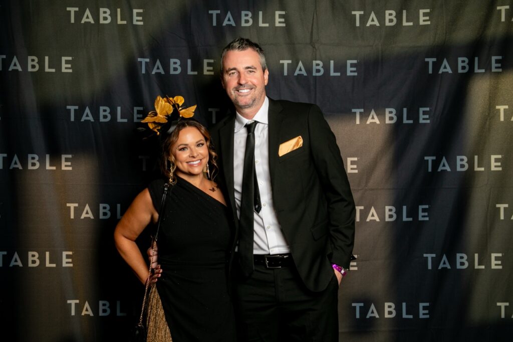Couple posing in front of a backdrop with "TABLE" repeated