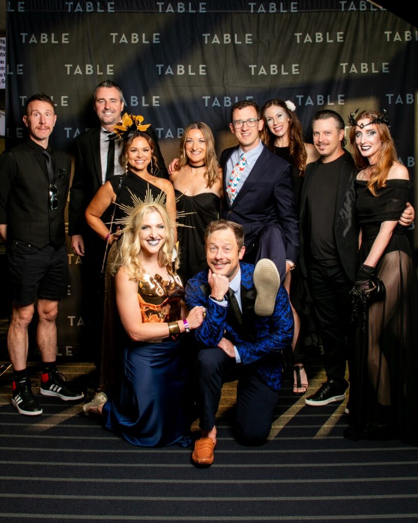 Group of ten people in formal attire posing in front of a TABLE backdrop