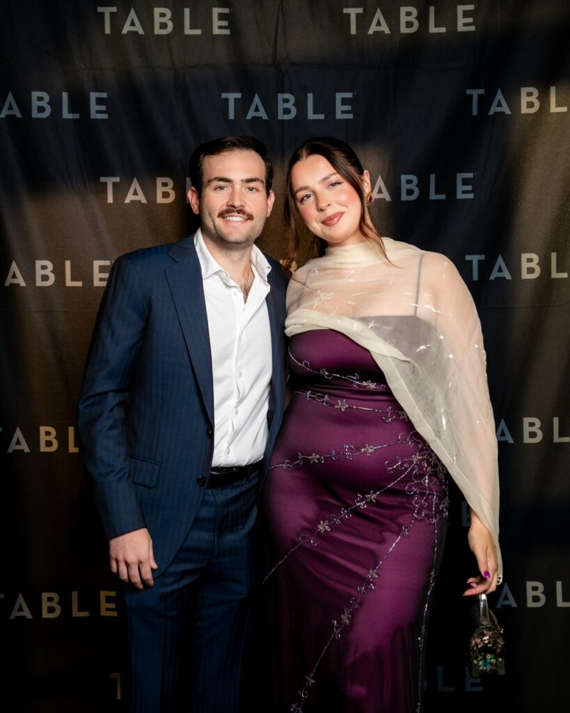 Couple posing in front of a "TABLE" backdrop at an event.
