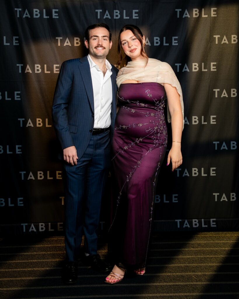 Couple posing in front of a black backdrop with "TABLE" logo