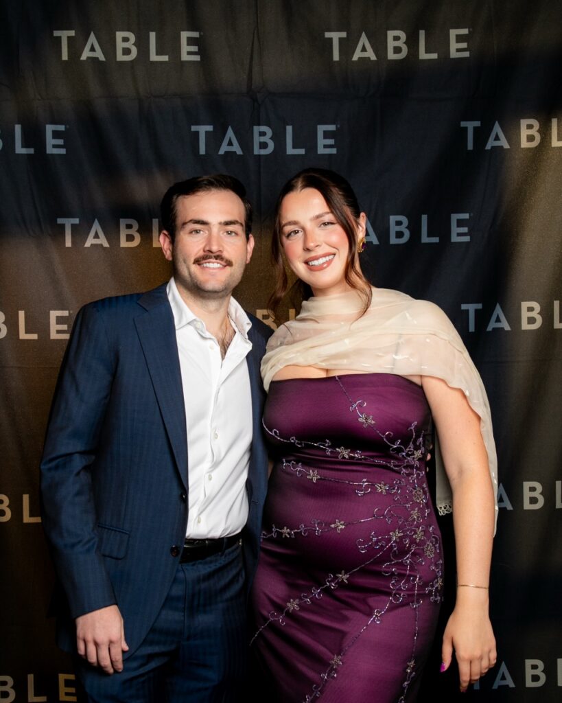 Couple posing in front of a TABLE backdrop at an event.