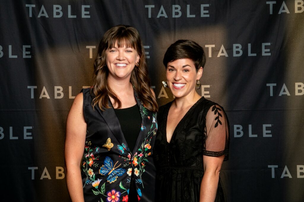 Two women smiling in front of a TABLE backdrop
