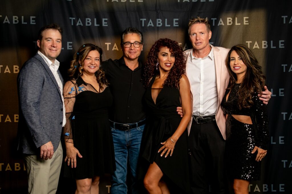Six people pose for a photo at a TABLE event, with the TABLE logo visible.