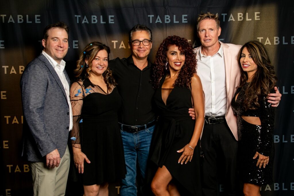 Six people pose for a photo at an event with "TABLE" branding in the background.
