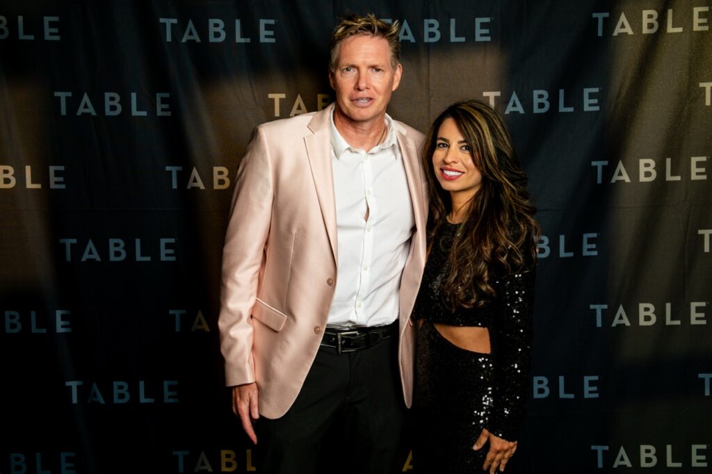 Man in pink blazer and woman in sequined dress pose for photo at TABLE event