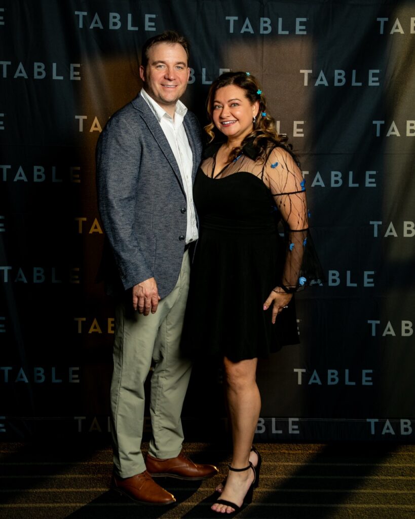 Couple posing in front of a "TABLE" backdrop at an event