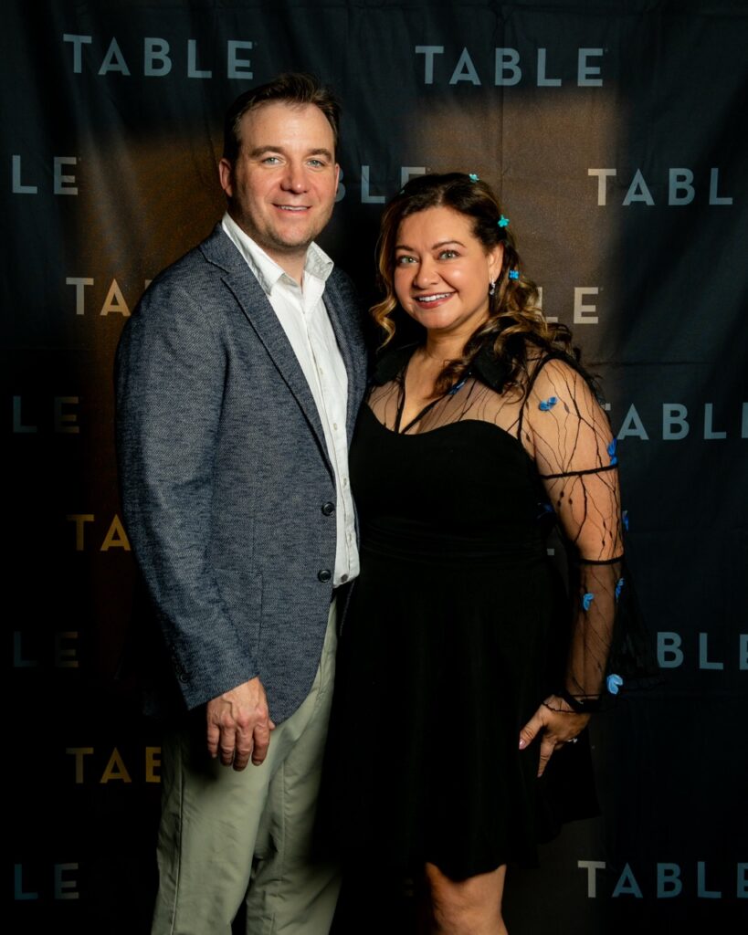 Couple posing in front of a black backdrop with "TABLE" logo