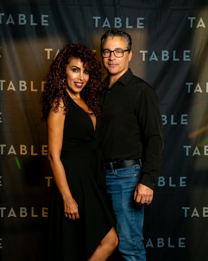 Couple posing in front of a black backdrop with "TABLE" logo