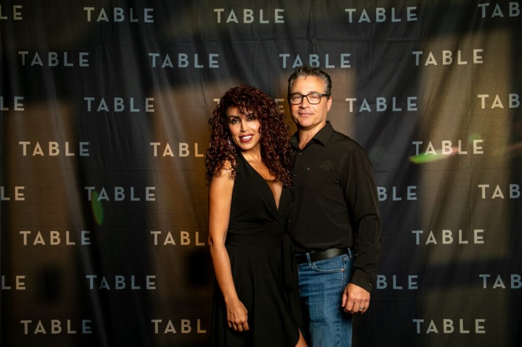 Couple posing in front of a backdrop with "TABLE" repeated