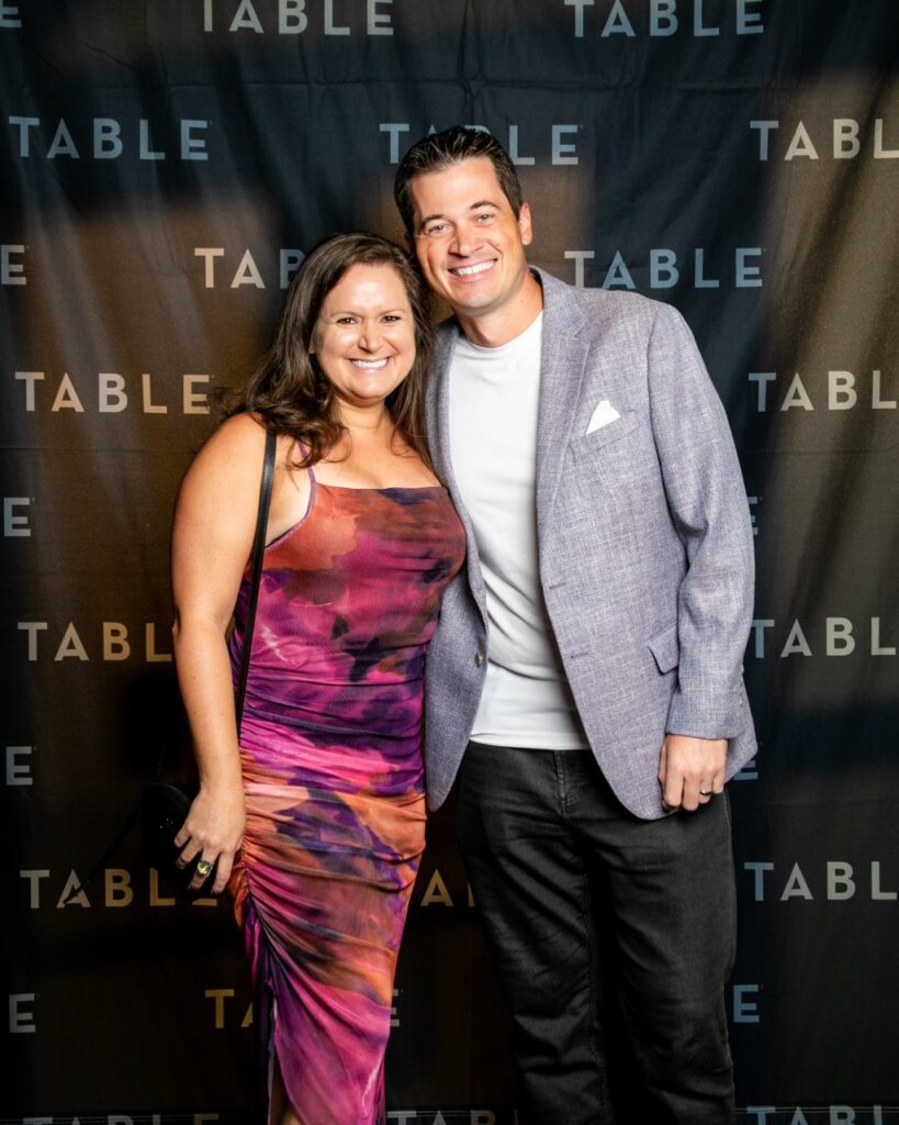 Couple smiling in front of a TABLE backdrop