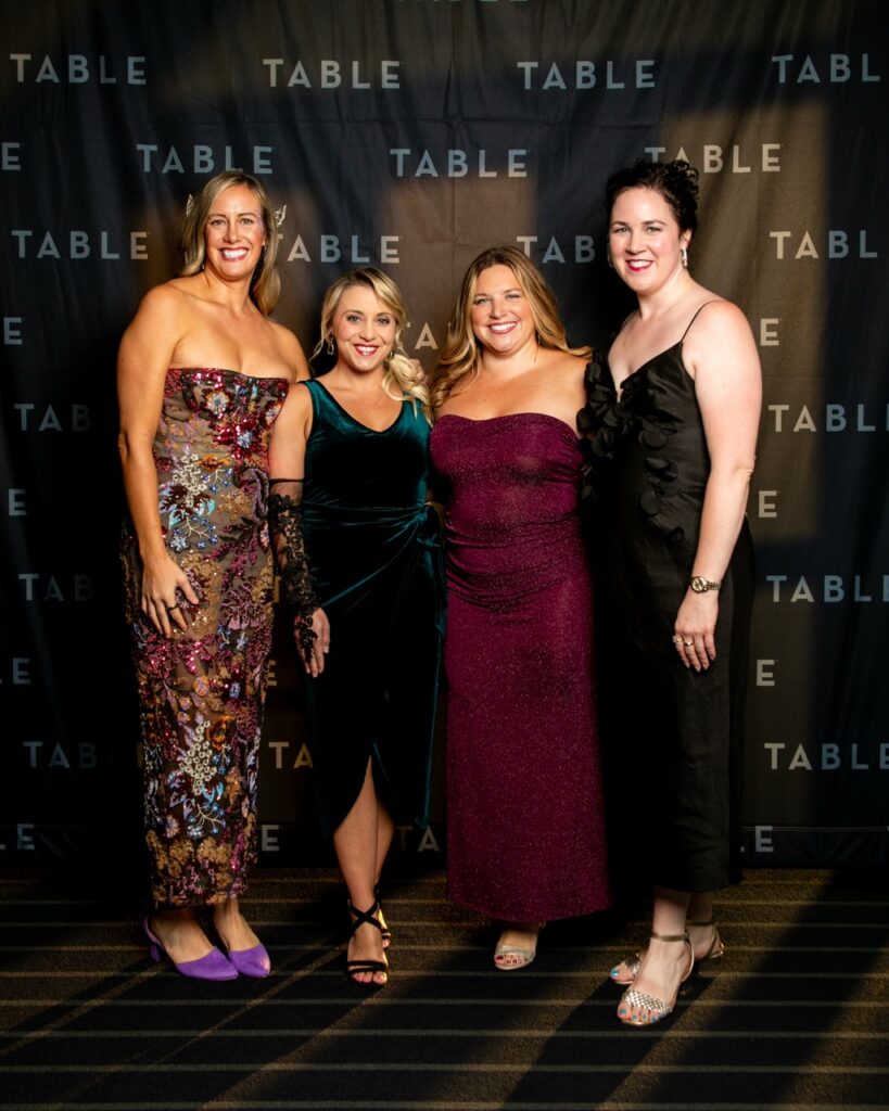 Four women in formal gowns pose for a photo at a TABLE event.