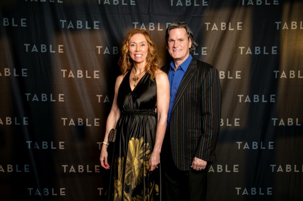 Couple posing in front of a TABLE backdrop at an event