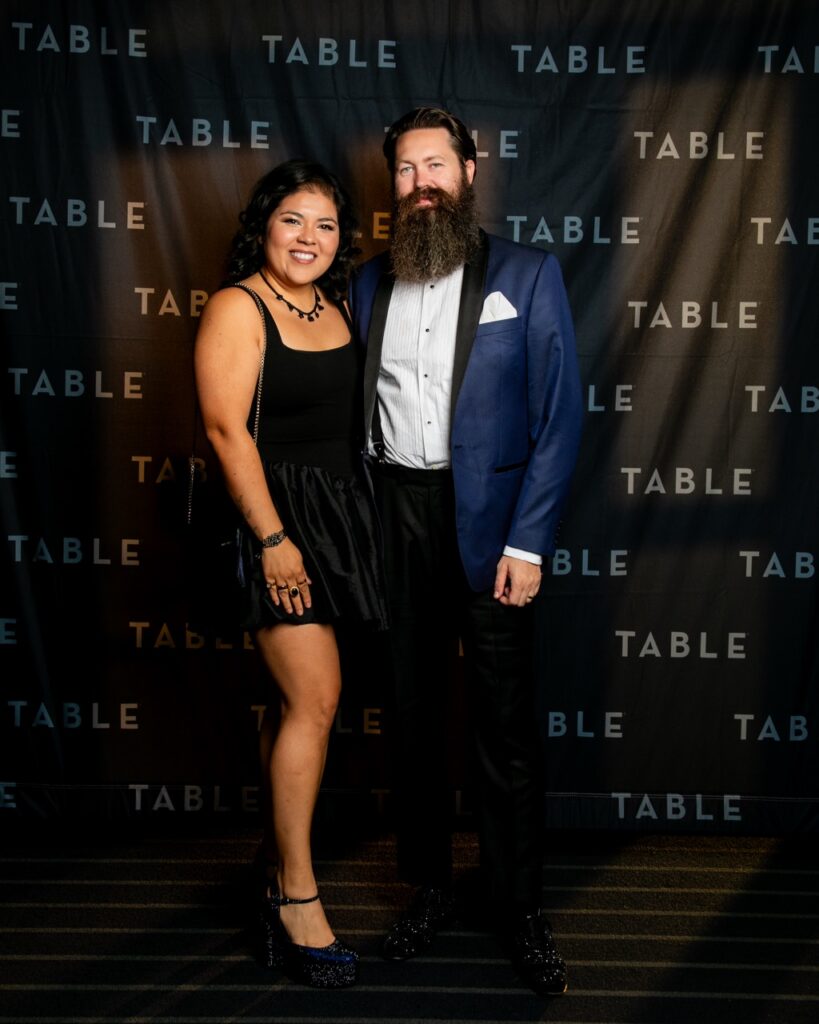 Couple posing for a photo in front of a backdrop with "TABLE" repeated