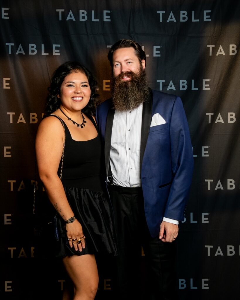 Couple posing in front of a black backdrop with "TABLE" logo