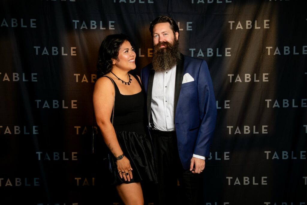 Couple posing in front of a "TABLE" backdrop at an event.