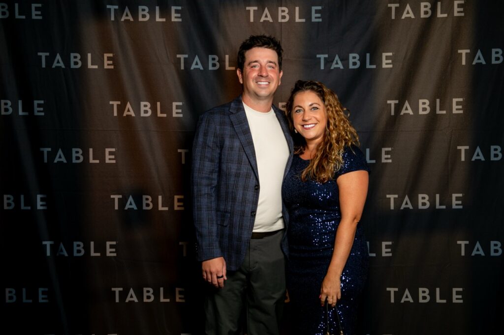 Couple posing in front of a TABLE backdrop at an event