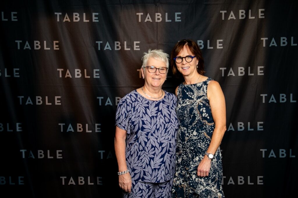 Two women smiling in front of a "TABLE" backdrop