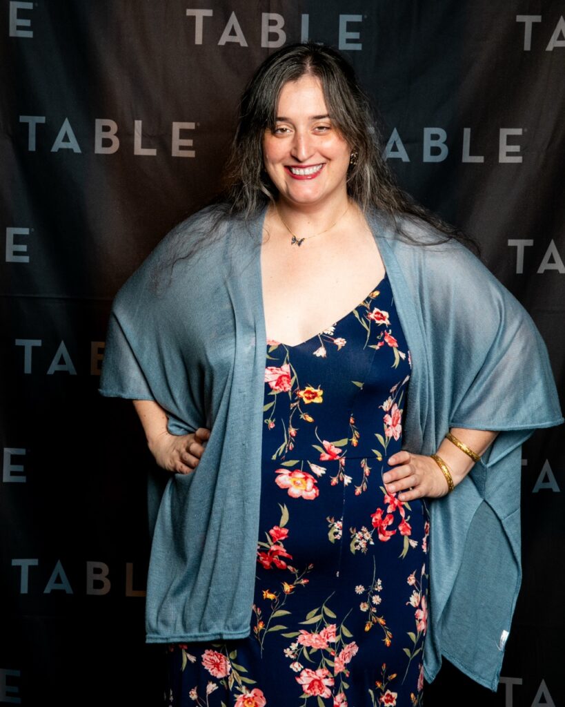Woman in floral dress and blue shawl smiles at the camera