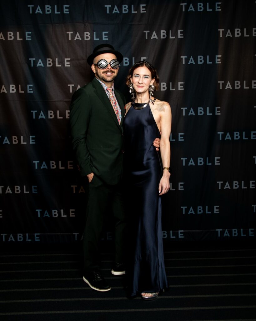 Couple in festive attire posing in front of a "TABLE" backdrop