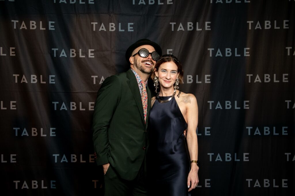 Couple poses at TABLE event with "TABLE" logo backdrop