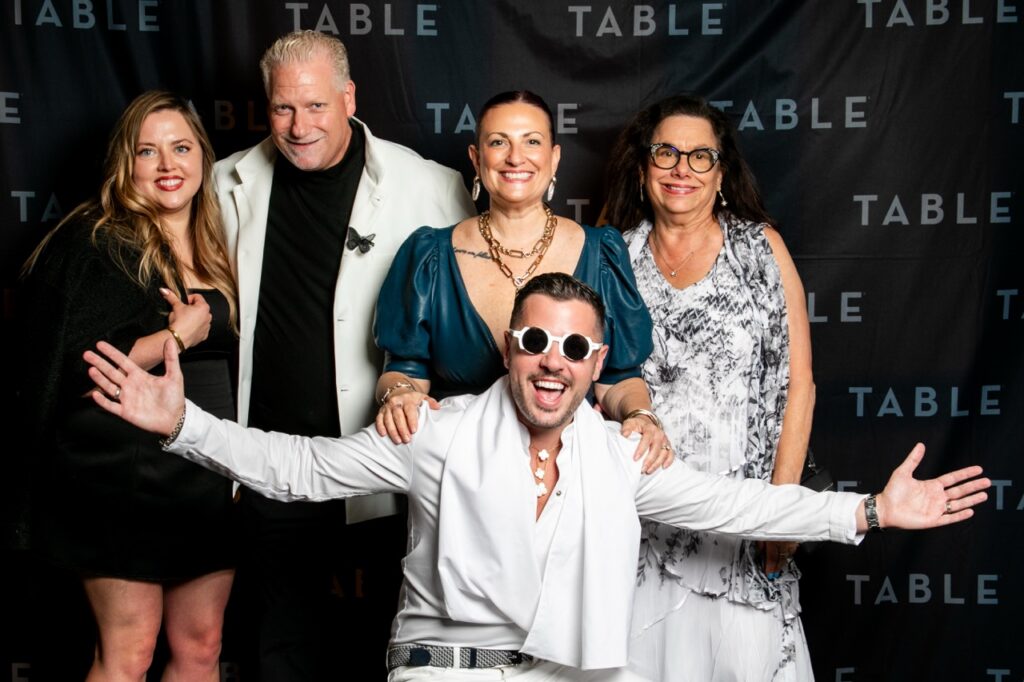Five people pose for a photo at an event with a TABLE backdrop.