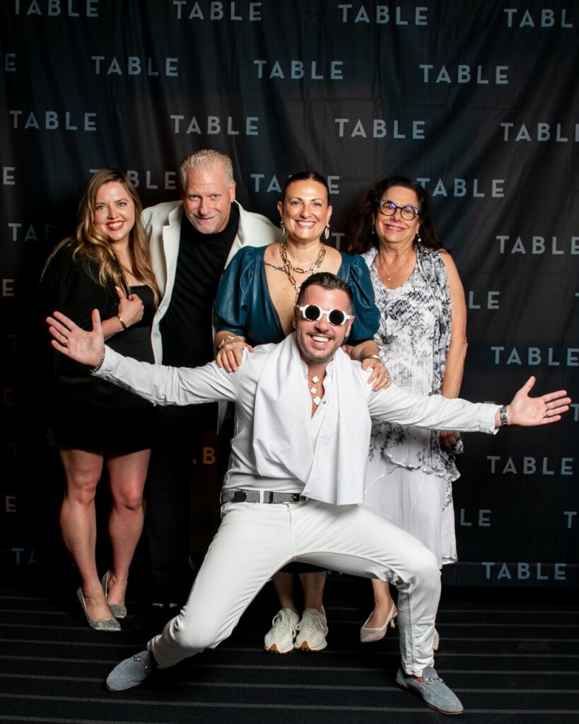 Five people pose for a photo in front of a backdrop with "TABLE" repeated.