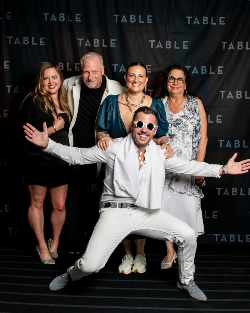 Group of people posing in front of a "TABLE" backdrop at an event