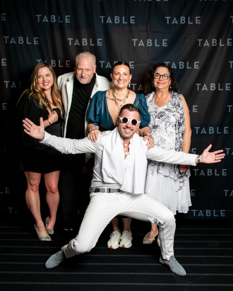 Group of five people posing for a photo in front of a backdrop with the word "TABLE" repeated.