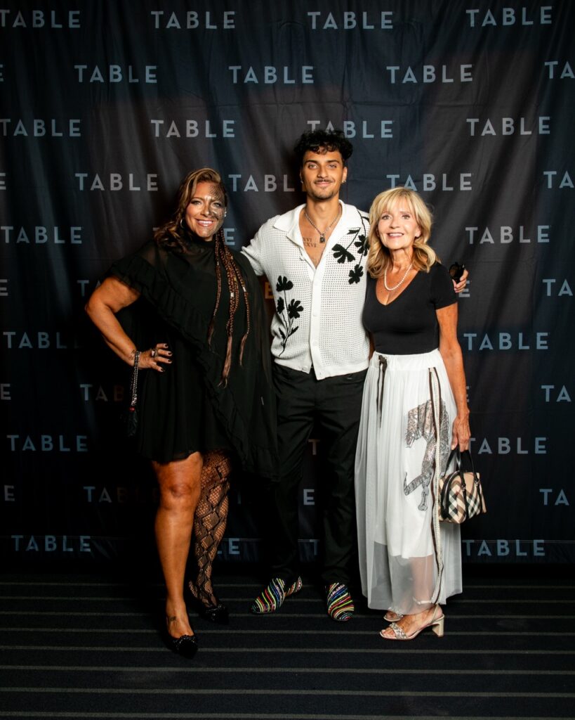 Two women and a man pose for a photo at an event with "TABLE" logos in the background.