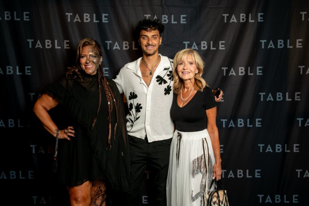 Three people pose for a photo in front of a black backdrop with "TABLE" logos.
