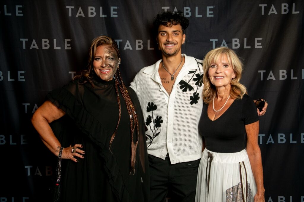 Three people pose for a photo in front of a "TABLE" backdrop.