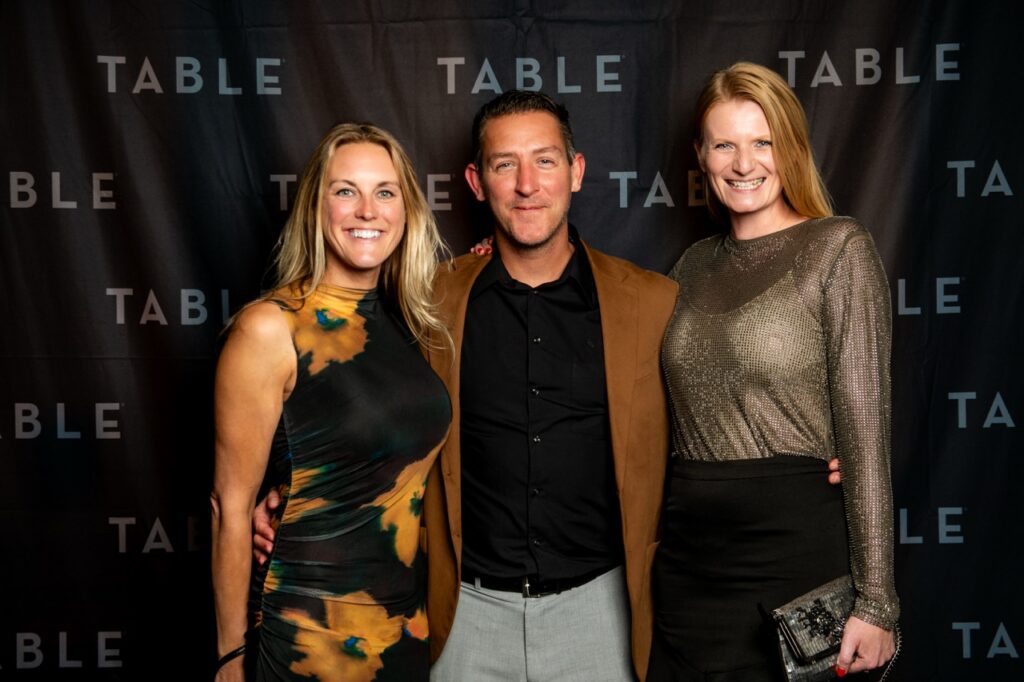 Three people posing for a photo in front of a TABLE backdrop
