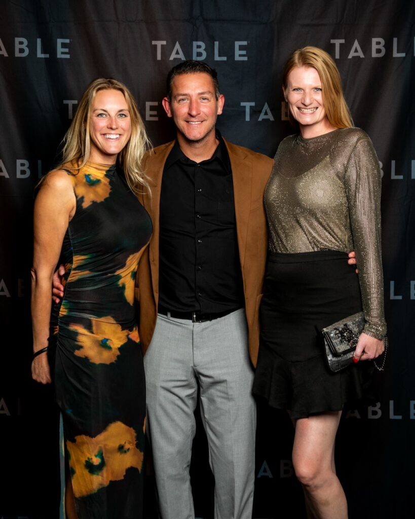 Three people posing for a photo at an event with a "TABLE" backdrop.