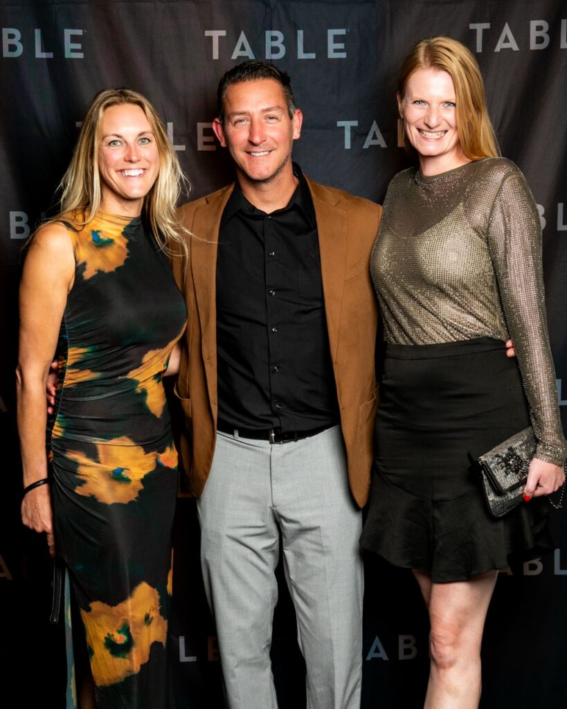 Three people pose for a photo at an event with "TABLE" logo in the background.