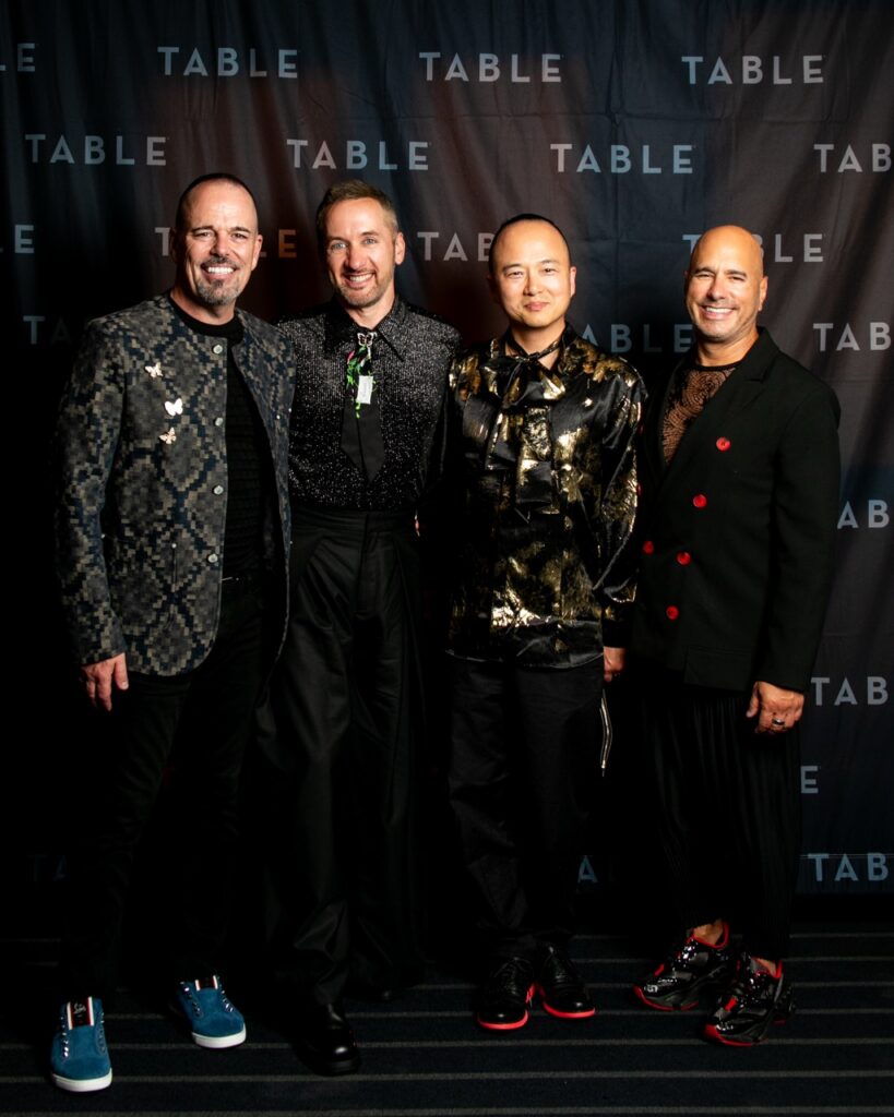 Four men in stylish outfits pose for a photo at an event with a "TABLE" backdrop.