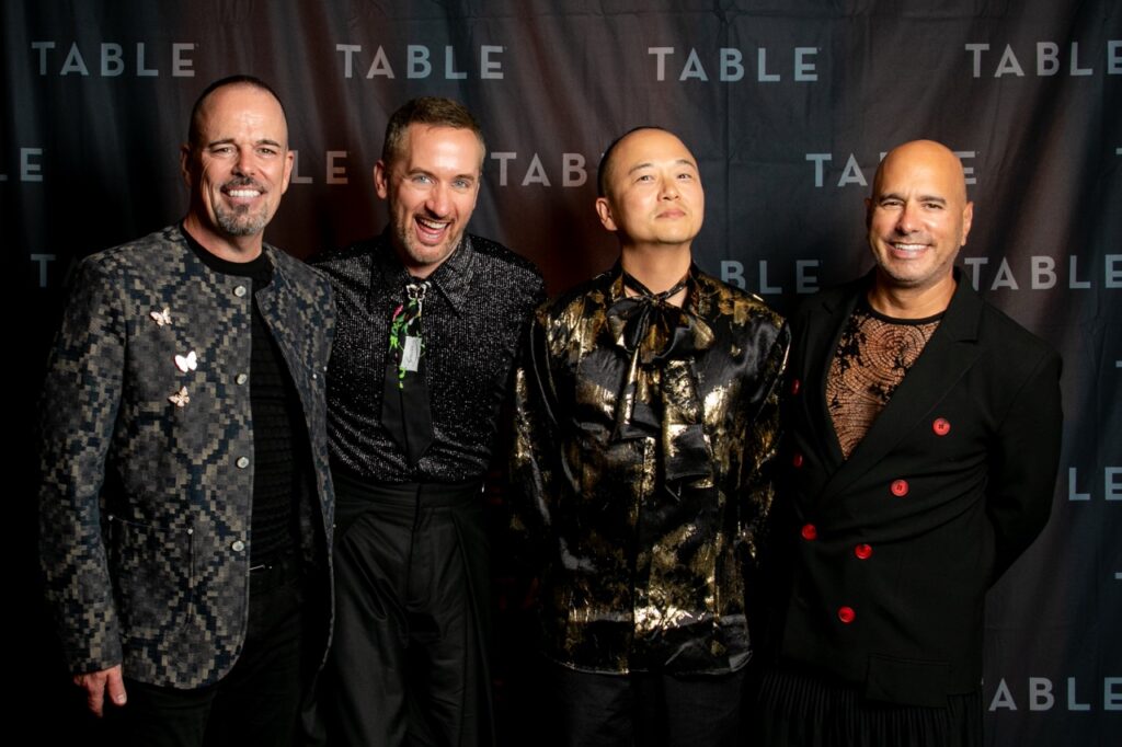 Four men in stylish outfits pose for a photo at an event with a "TABLE" backdrop.