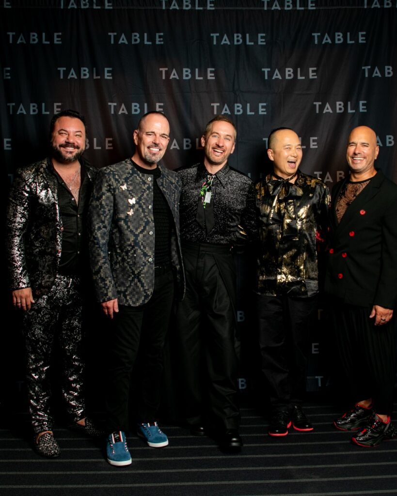 Five men in stylish outfits pose for a photo at an event with "TABLE" branding.